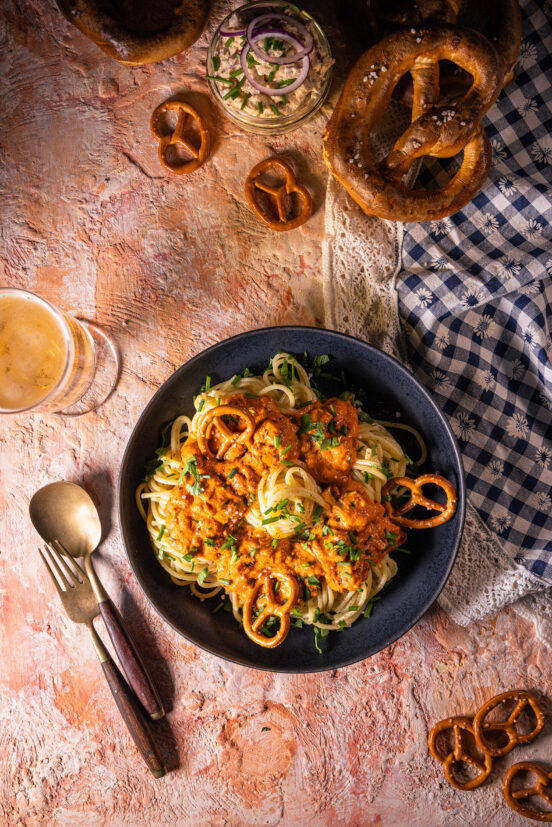 Spaghetti al Camembert – Pasta mit Obazda-Sauce - vegan - mit kleinen Brezeln auf einem Teller. NOch mehr Brezeln auf dem Tisch.