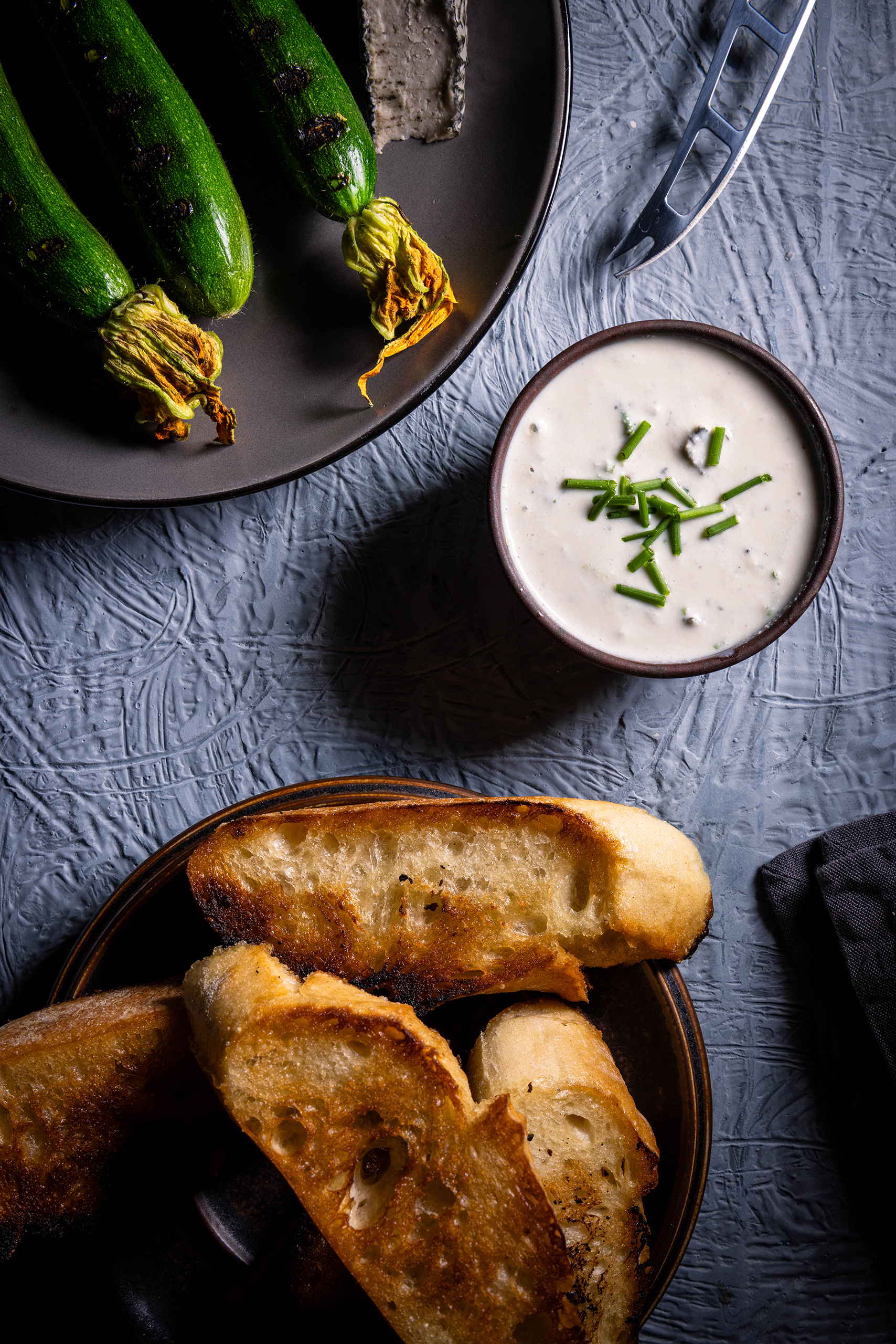 Veganer Blauschimmelkäsedip– in einer Schale, daneben ein Teller mit gerösteten Babyzucchini und ein Teller mit geröstetem Brot.
