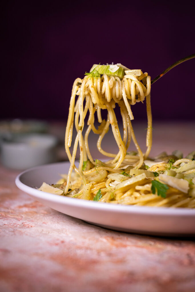 Fenchel Spaghetti angerichtet auf einem Teller und auf eine Gabel aufgewickelt, welche die Sapghetti in der Luft hält.