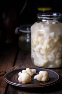 Fermentierter Blumenkohl - drei Röschen auf einem Teller und das Fermentierglas dahinter.
