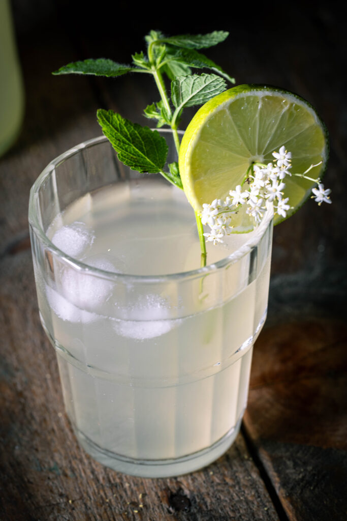 Holunderkefir in einem Glas mit Limettenscheibe, Holunderblüten nd Minzstengel
