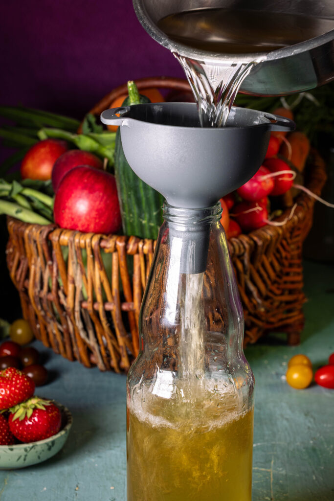 Holunderessig wird mit einem Trichter in eine Flasche gefüllt.