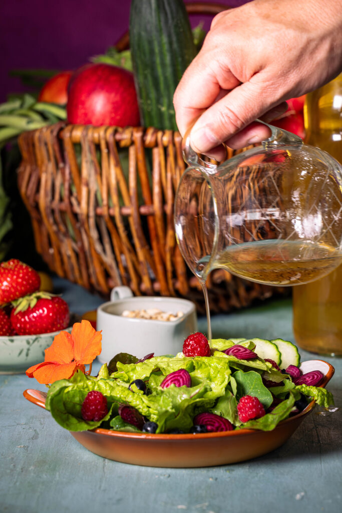 Eine Vinaigrette mit Holunderessig wird aus einer Karaffe über einen Salat gegeben.