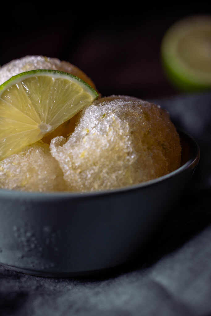 Kombucha-Limetten-Sorbet - drei Kugeln in einer grünen Schale. Mit einer Scheibe Limette.
