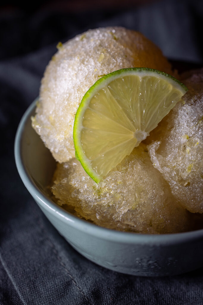 Kombucha-Limetten-Sorbet - drei Kugeln in einer grünen Schale. Mit einer Scheibe Limette.