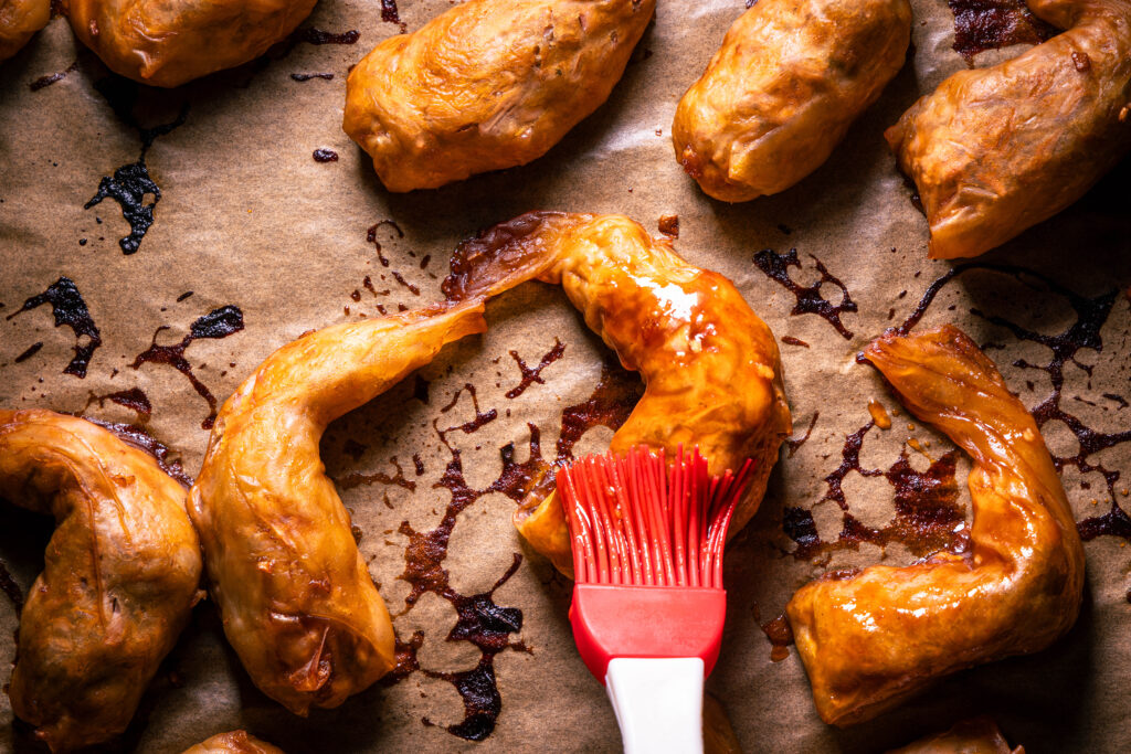 Halb gebackene, vegane Sticky Wings werden mit Marinade eingepinselt.