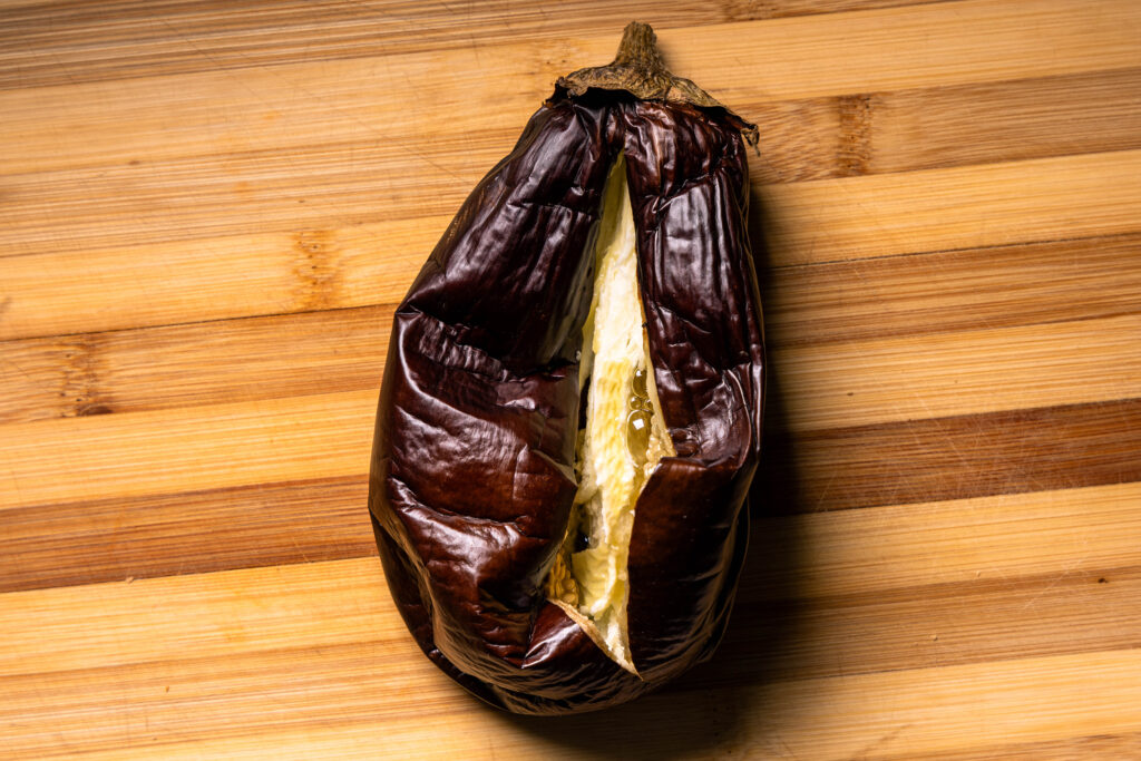 Eine offene, gegrillte Aubergine auf einem Holzbrett.