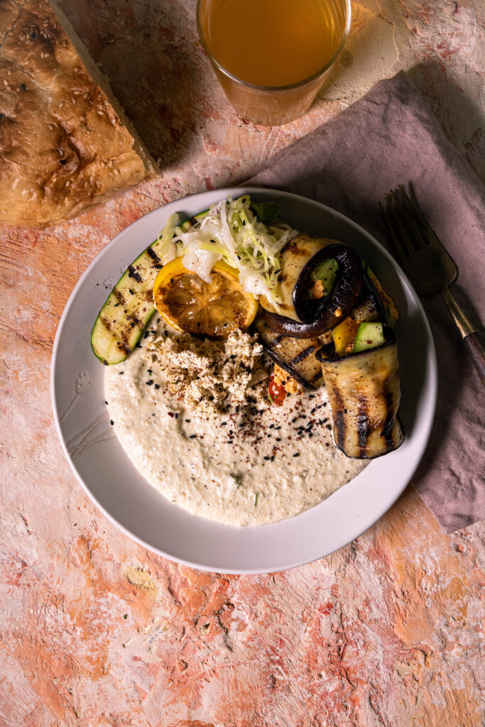 Veganer Auberginen-Schafskäse-Dip, Auberginen-Veta-Creme, mit verschiedenen Beilagen auf einem Teller.