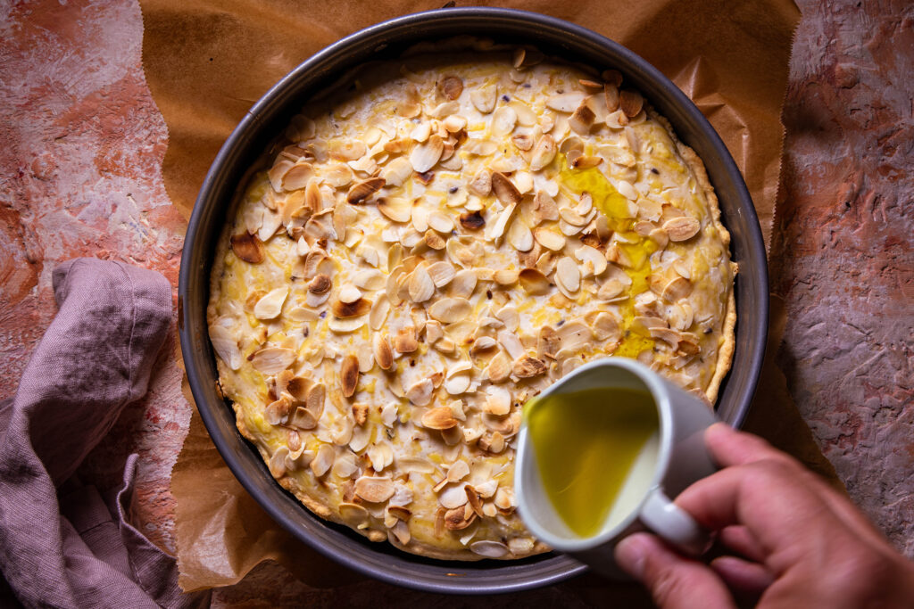 Halbfertig gebackene Quiche wird mit Olivenöl besprenktelt.