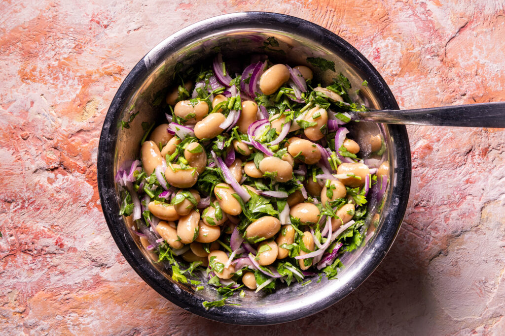 Türkischer Weiße Bohnensalat wird in einer Schüssel angerührt.