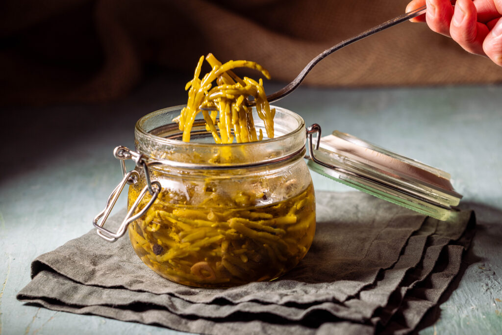 Salicorne Pickles - eingelegter Meerspargel - in einem Glas, eine Gabel holt eine Portion heraus.