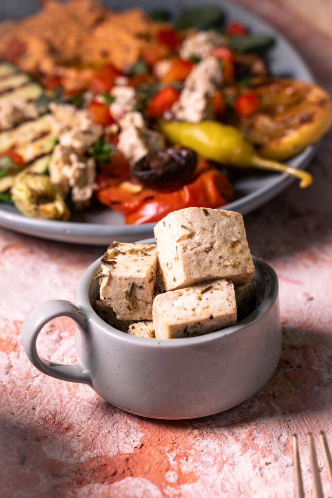 Veganer Feta (Veta). Im Hintergrund verarbeitet in veganem, scharfen Schafskäse Dip mit Anti Pasti.