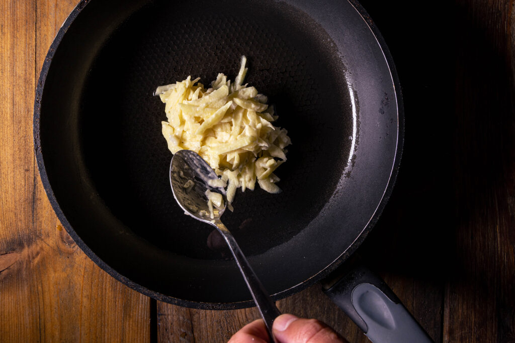 Pufferteig wird esslöffelweise in eine Pfanne gegeben.