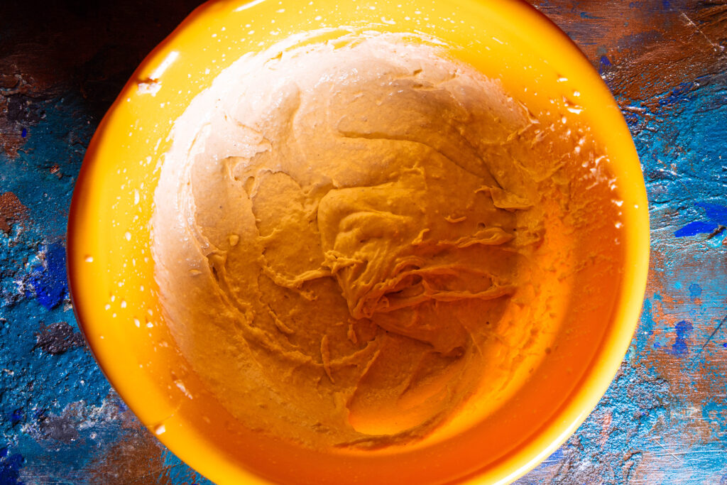 Waffelteig wird in einer orangen Teigschüssel gemixt.