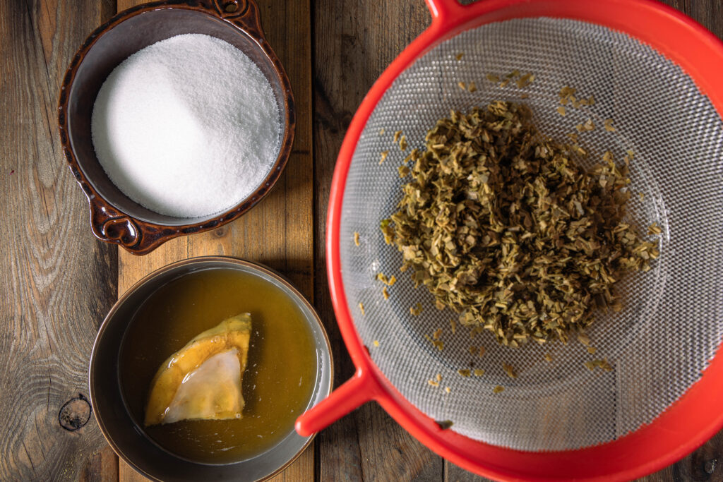 Mate-Tee wird abgeseiht, daneben eine Schale mit Zucker und eine mit einem Scoby.