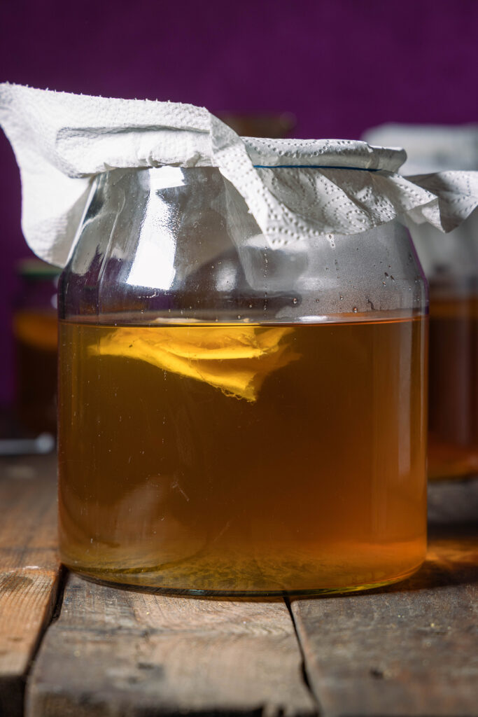 Kombucha fermentiert in Mate-Tee in einem großen, abgedeckten Glasgefäß.