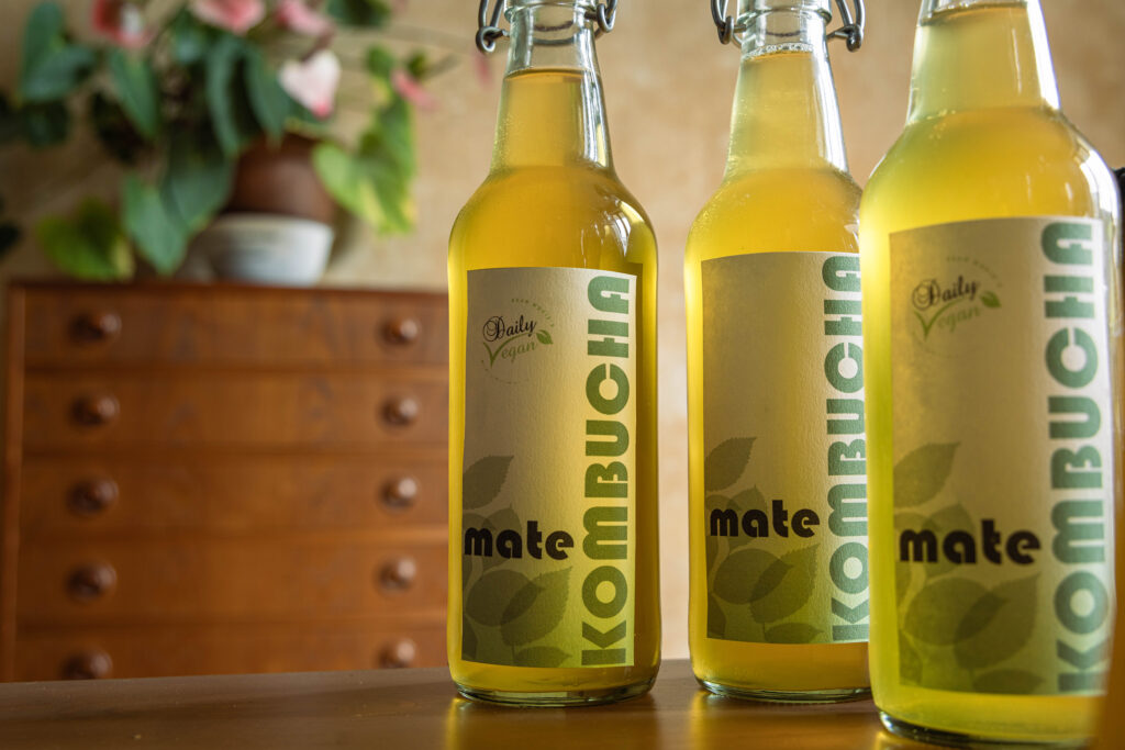 Drei Flaschen mit Kombucha aus Matetee stehen auf einem Tisch.
