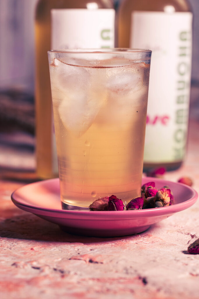 Rosenkombucha mit Eiswürfeln in einem Glas. Daneben getrocknete Rosenknospen.