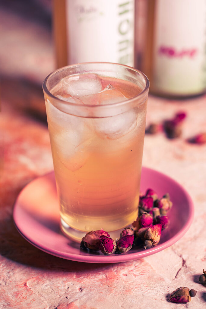 Rosenkombucha mit Eiswürfeln im Glas, daneben getrocknete Rosenknospen.