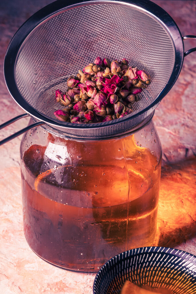 Mit Rosen aroatisiertes Wasser wird in ein großes Glasgefäß abgeseiht.