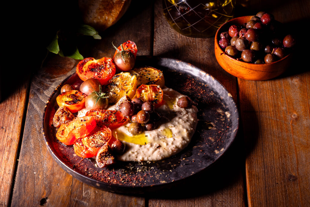 Schlehenoliven mit gegrillten Tomaten und Zitronenscheiben auf würzigem Weiße-Bohnen-Dip mit Salzzitrone.