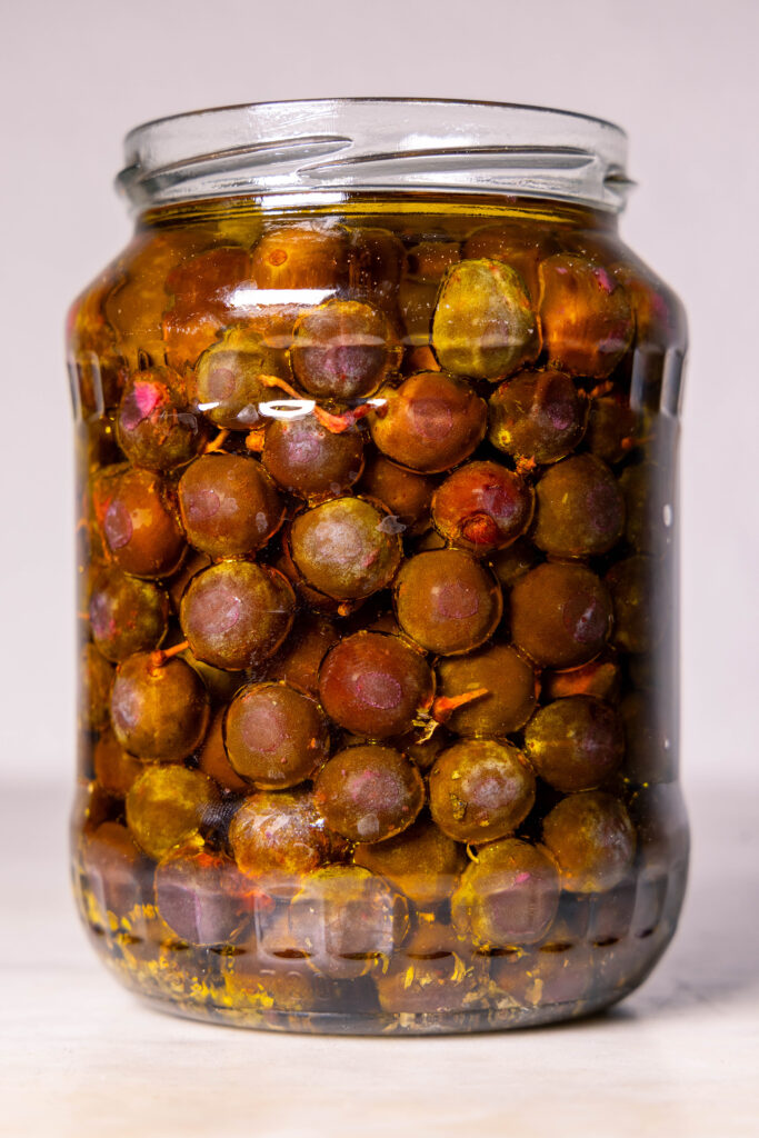 Fermentierte Schlehen mit Kräutern in Olivenöl eingelegt in einem Schraubglas.