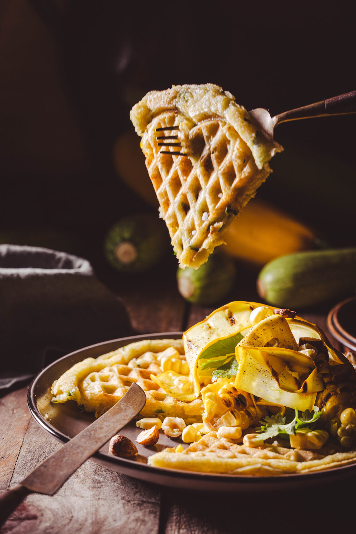 Zucchini-Mais-Waffeln - herzhafte Waffeln - mit Toppings auf einem Teller und auf einer Gabel aufgespießt.