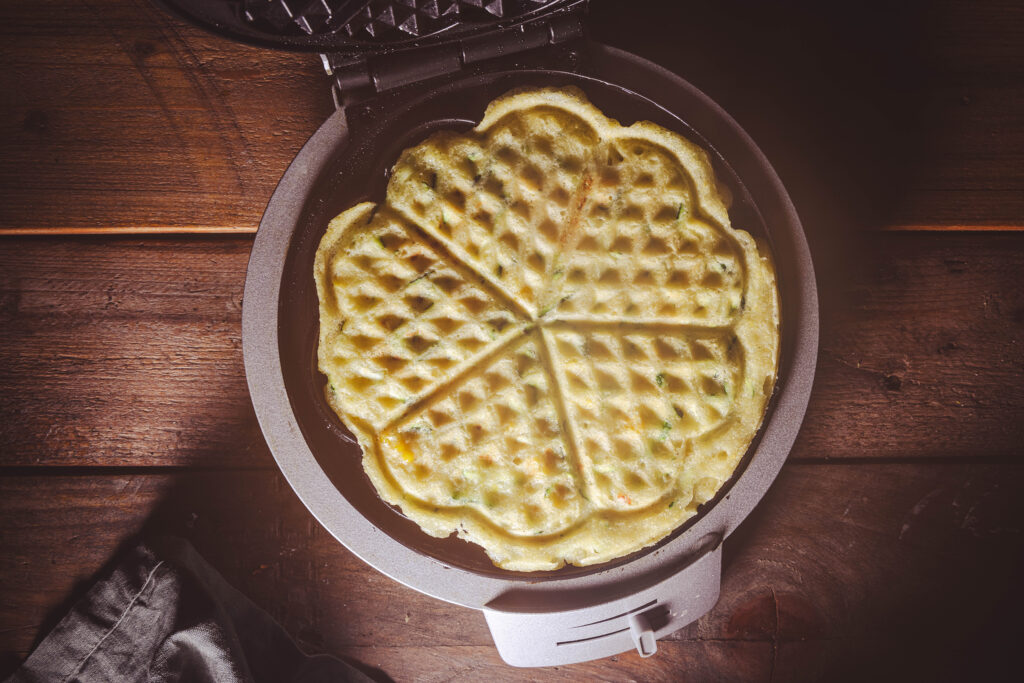 Eine vegane Zucchini-Mais-Waffel backt im Waffeleisen.