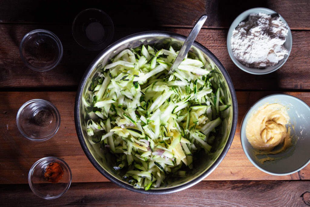 Eine Schüssel mit geriebenen Zucchini, Kartoffeln und gewürfelten Schallotten.