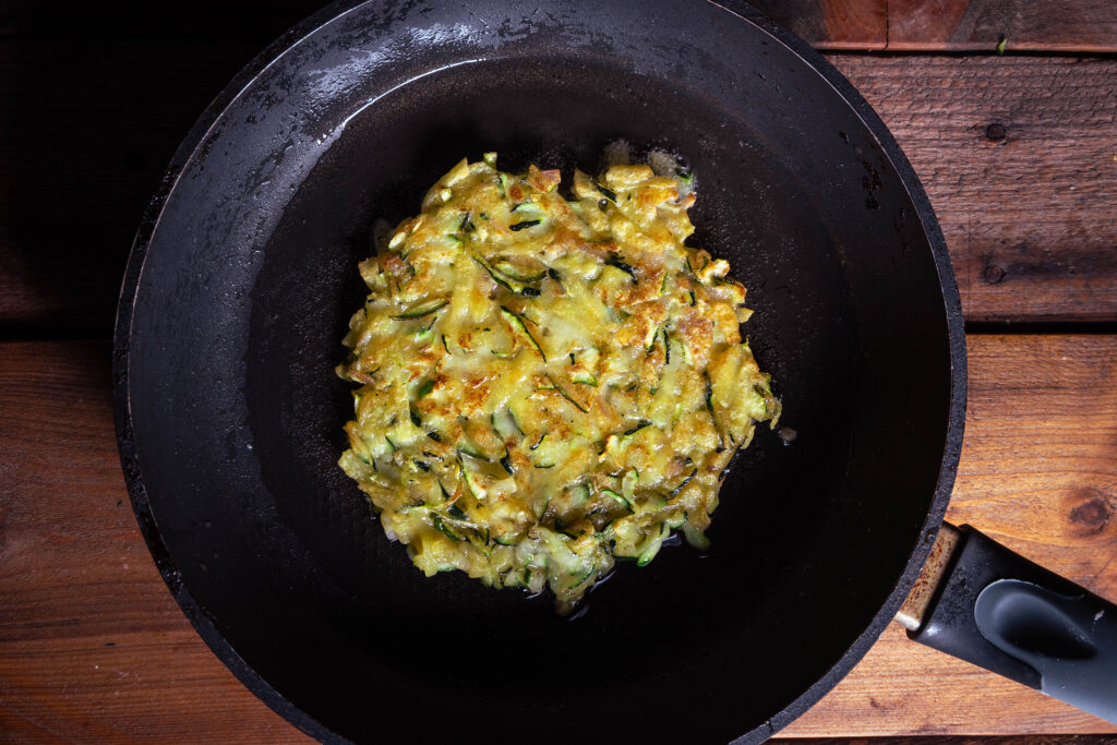 Ein Zucchini-Puffer brät in einer Pfanne.