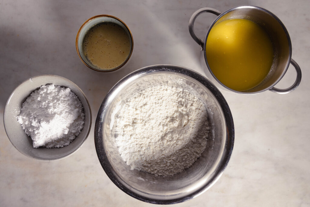 Vegane Butter, geschmolzen in einem kleinen Topf. Mehlgemisch und weitere Zutaten in Schalen.