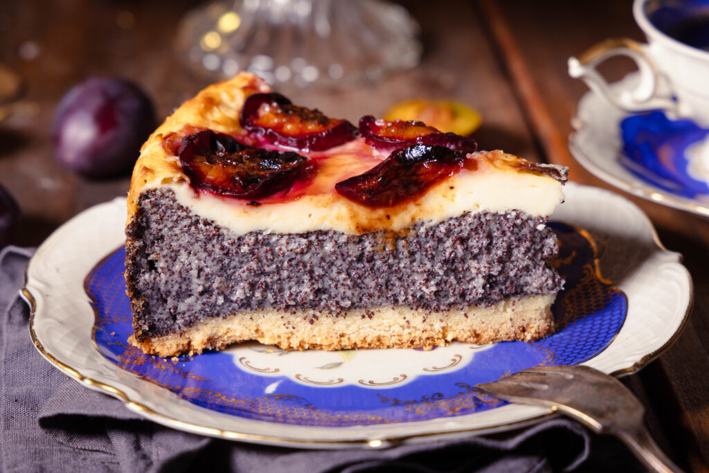 Zwetschen-Mohn-Käsekuchen auf einem Sammeltassenteller. Mit Sammeltasse im Hintergrund.