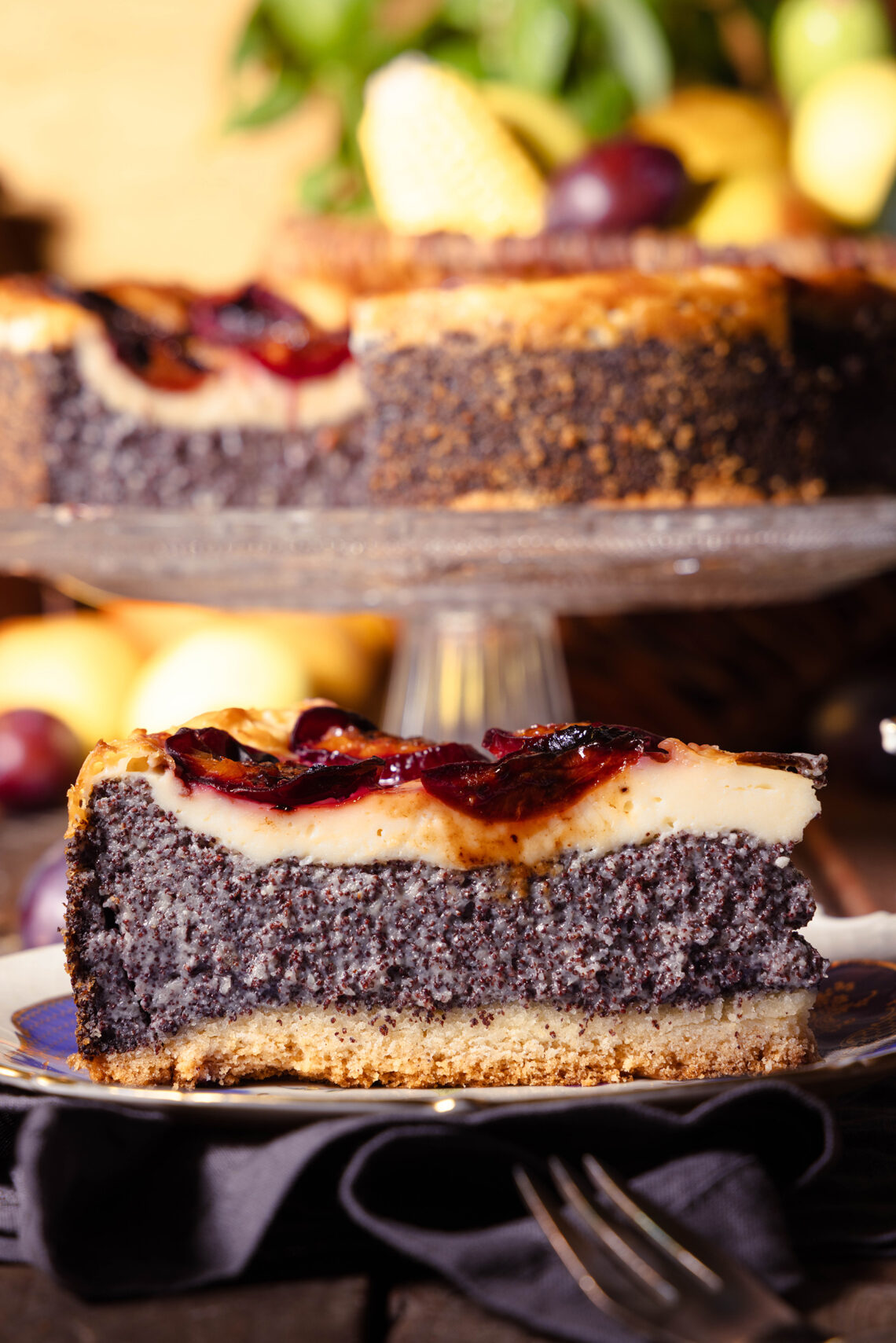 Zwetschen-Mohn-Käsekuchen, ein Stück auf einem Teller, der restliche Kuchen im Hintergrund
