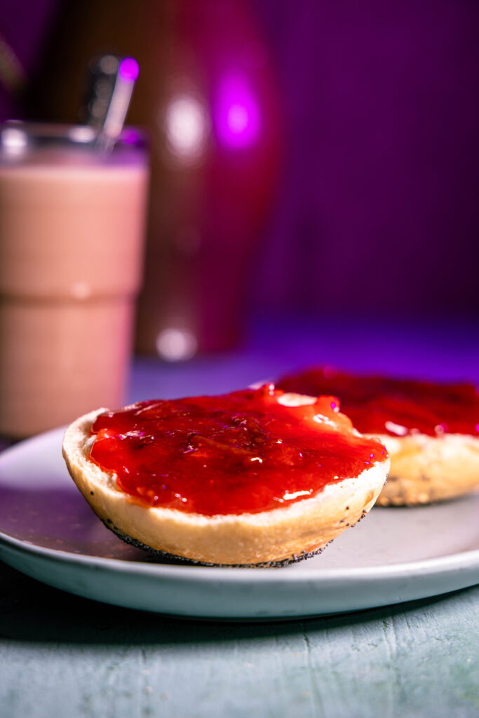Ein Brötchen, mit Zwetschenmus bestrichen. Dshinter ein Glas Kakao.
