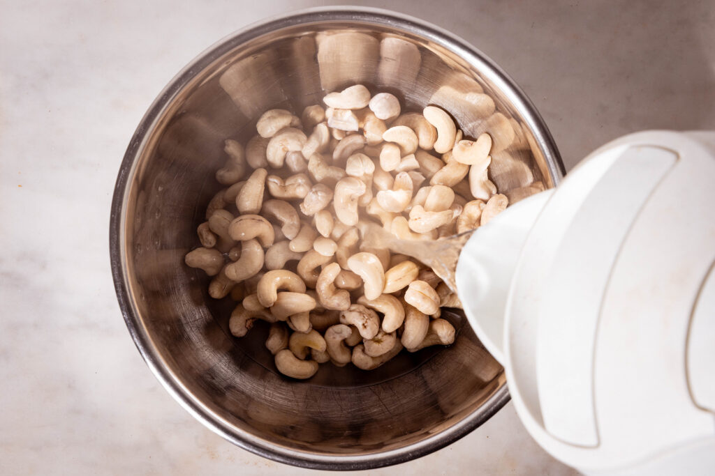 Aus einem Wasserkocher wird Wasser in eine Schale mit Cashewkernen gegossen.