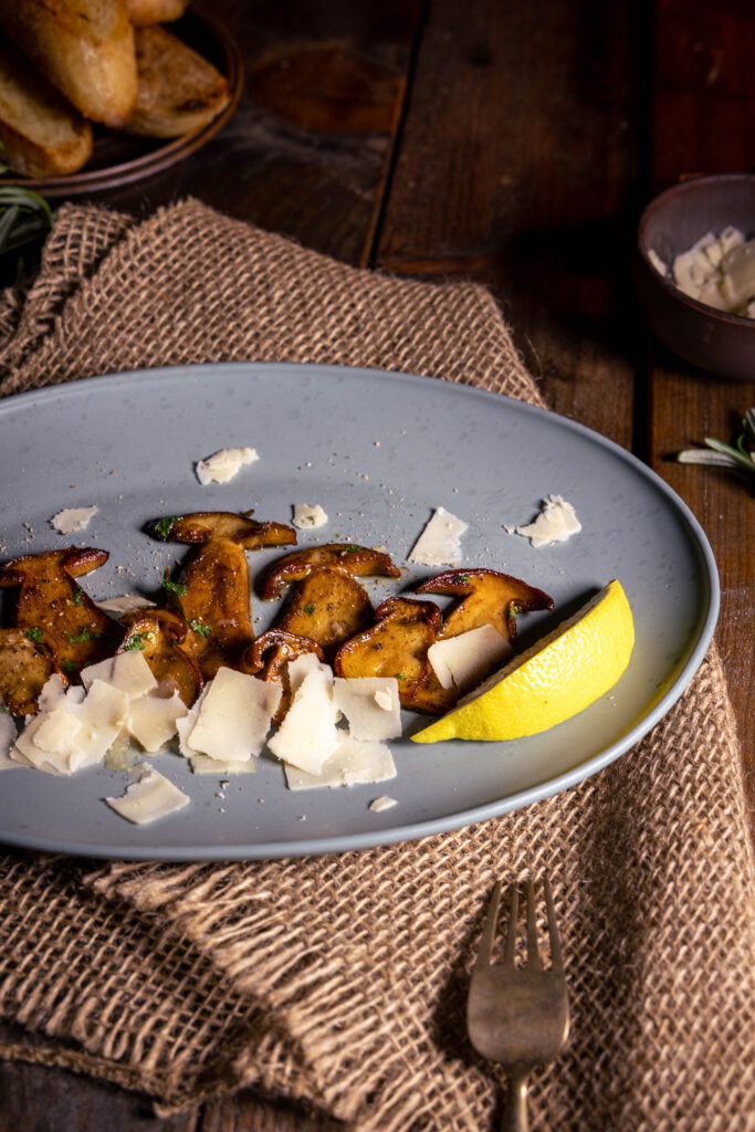 Gebratene Steinpilze mit veganem Parmesan und einem Schnitzer Zitrone auf einem Teller.