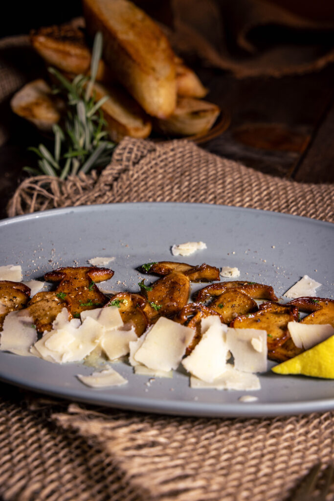 Gebratene Steinpilze mit veganem Parmesan und einem Schnitzer Zitrone auf einem Teller.