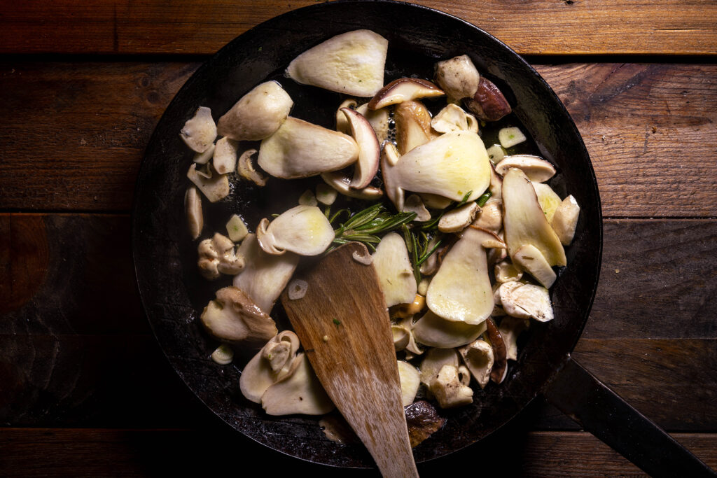 Steinpilze, Rosmarinzweig und Knoblauch braten in einer Pfanne mit Olivenöl.