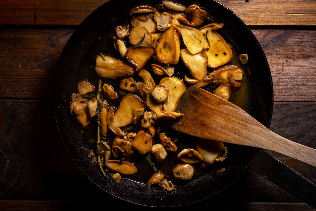 Steinpilze, Rosmarinzweig, Weißwein und Knoblauch braten in einer Pfanne mit Olivenöl.
