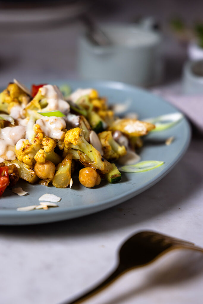 Gerösteter Blumenkohlsalat auf einem Teller, dahinter Schüsselchen mit Beilagen.
