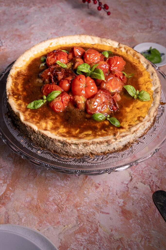 Veganer herzhafter Käsekuchen mit Rösttomaten-Topping bereit zum Anschneiden.