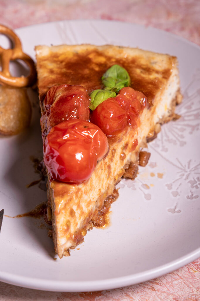 Herzhafter Käsekuchen mit Rösttomaten-Topping – vegan - ein Stück auf einem Teller.