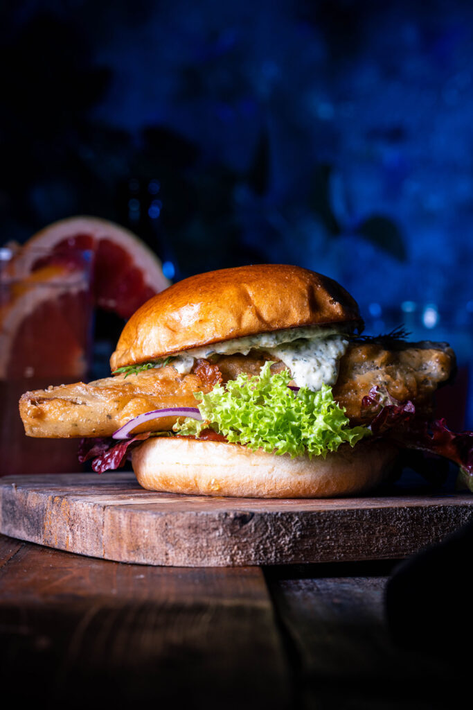 No Catch Fishburger – der beste vegane Fischburger auf einem Holzbrett, dahinter Getränke