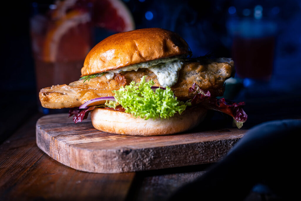 No Catch Fishburger – der beste vegane Fischburger auf einem Holzbrett, dahinter Getränke