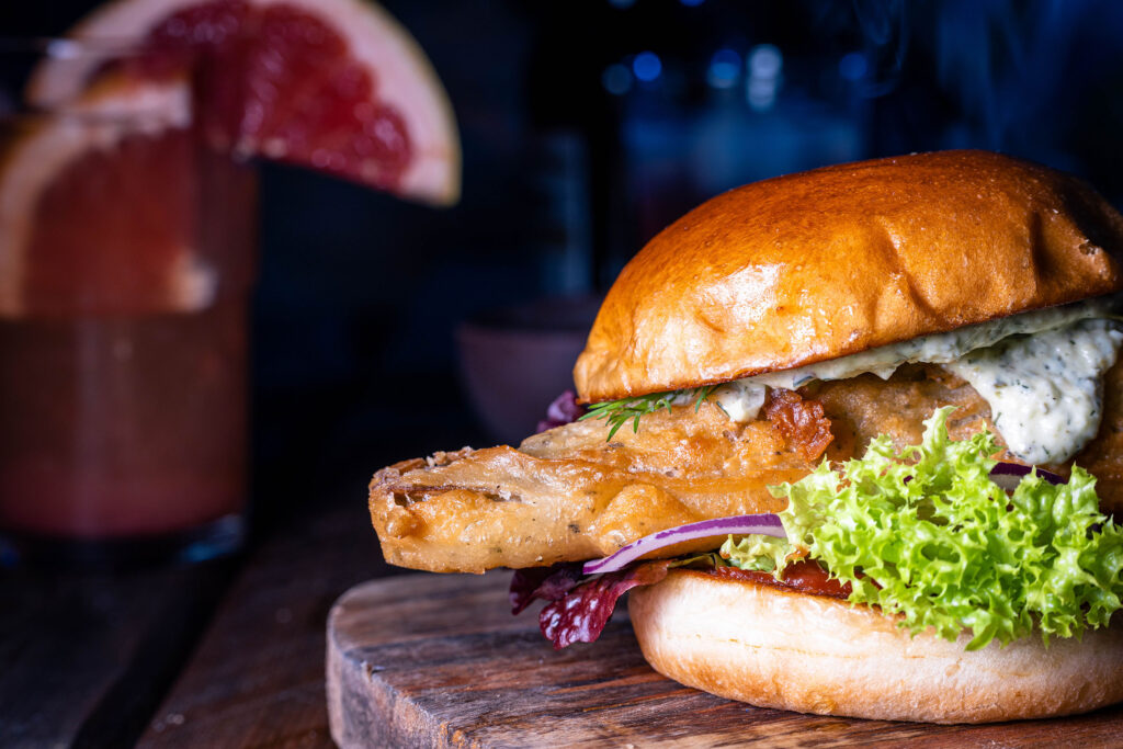 No Catch Fishburger – vegane Fischburger auf einem Holzbrett. Dahinter ein Getränk mit Grapefruit.
