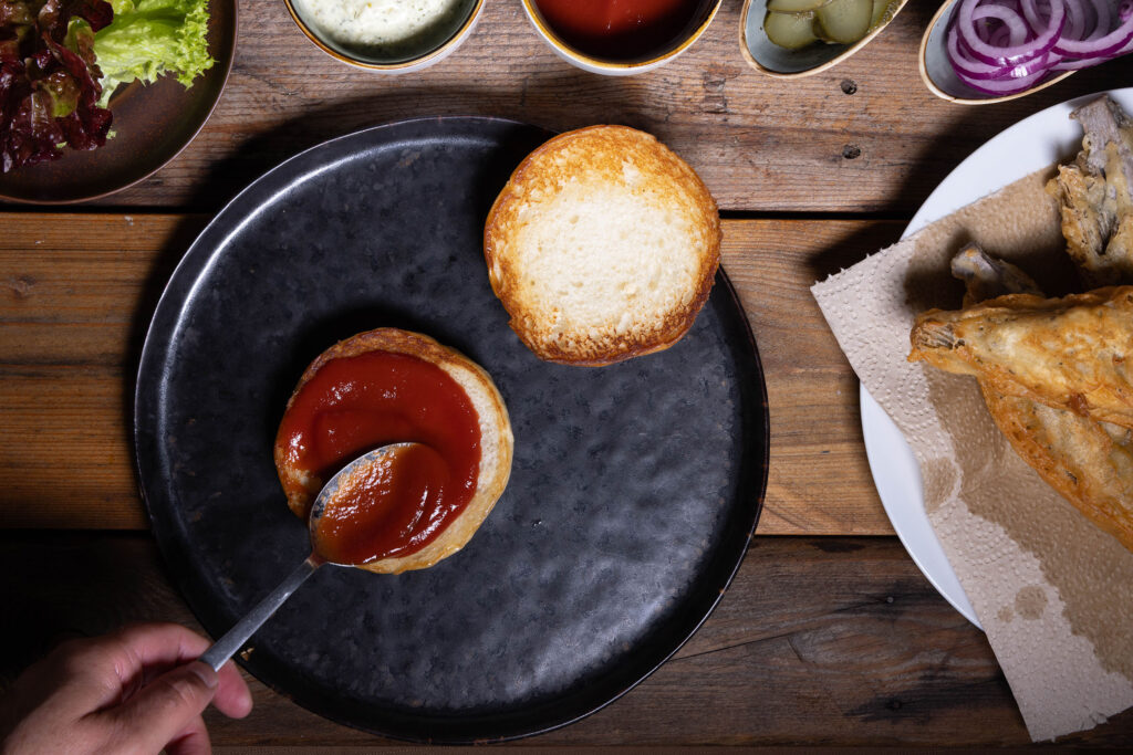 Ein Burgerbrötchen wird mit Ketchup bestrichen.