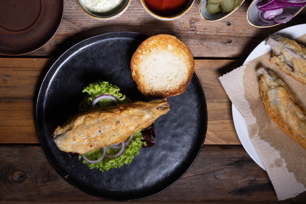 Ein Burger wird mit veganem Backfisch belegt.