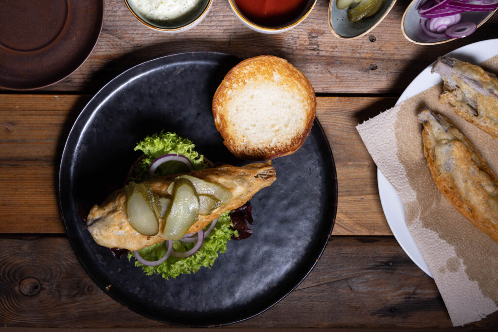 Ein veganer Fischburger wird mit sauren Gurken belegt.