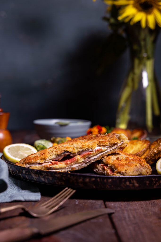 Parasol Cordon Bleu , aufgeschitten auf einem Teller. Dahinter eine Sonnenblume in iner Vase.