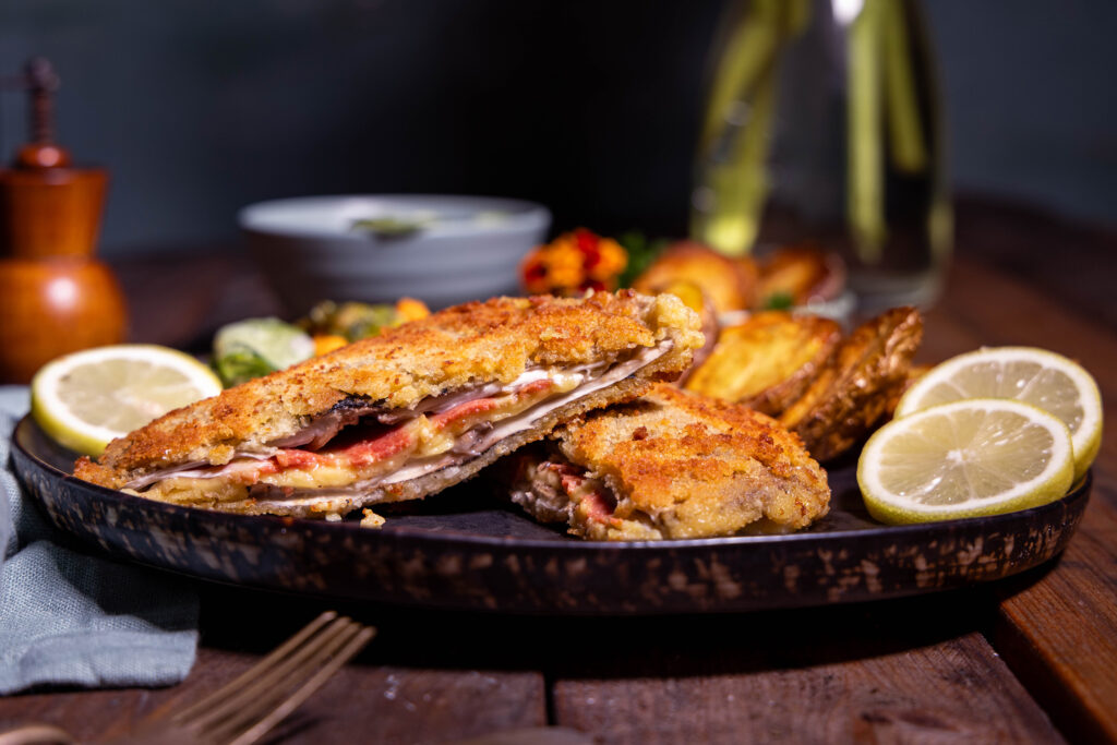 Parasol Cordon Bleu – aufeschnitten auf einem Teller mit Zitronenschnitzen und Beilagen.